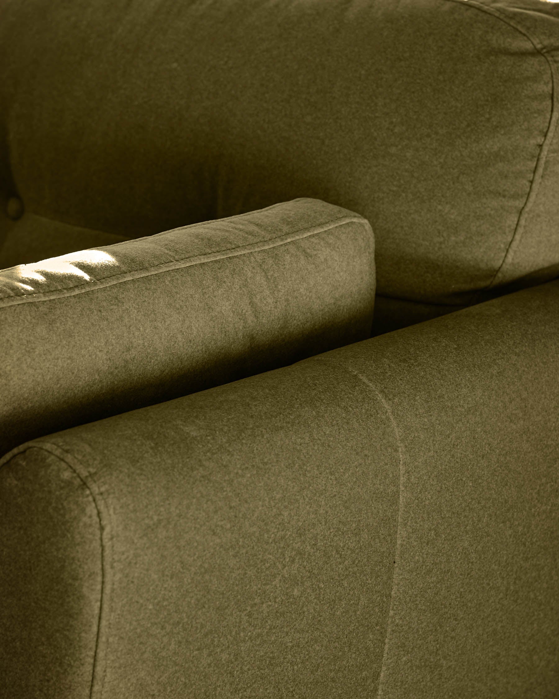 Pistachio green fabric armchair detail showing upholstered arm and seat cushion with stitched seams in natural daylight.