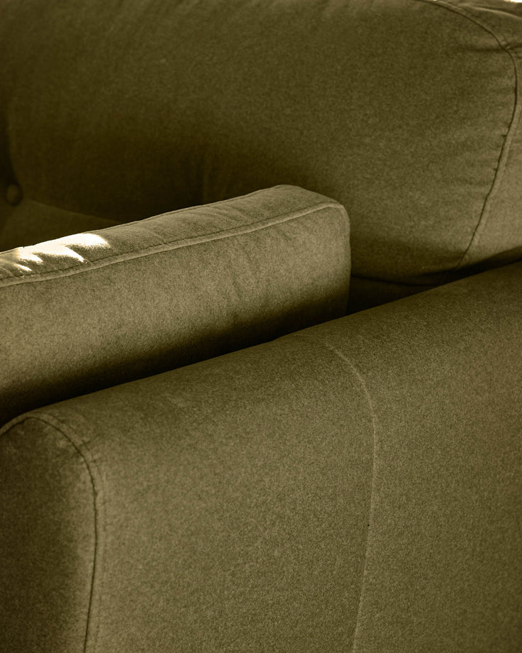Pistachio green fabric armchair detail showing upholstered arm and seat cushion with stitched seams in natural daylight.