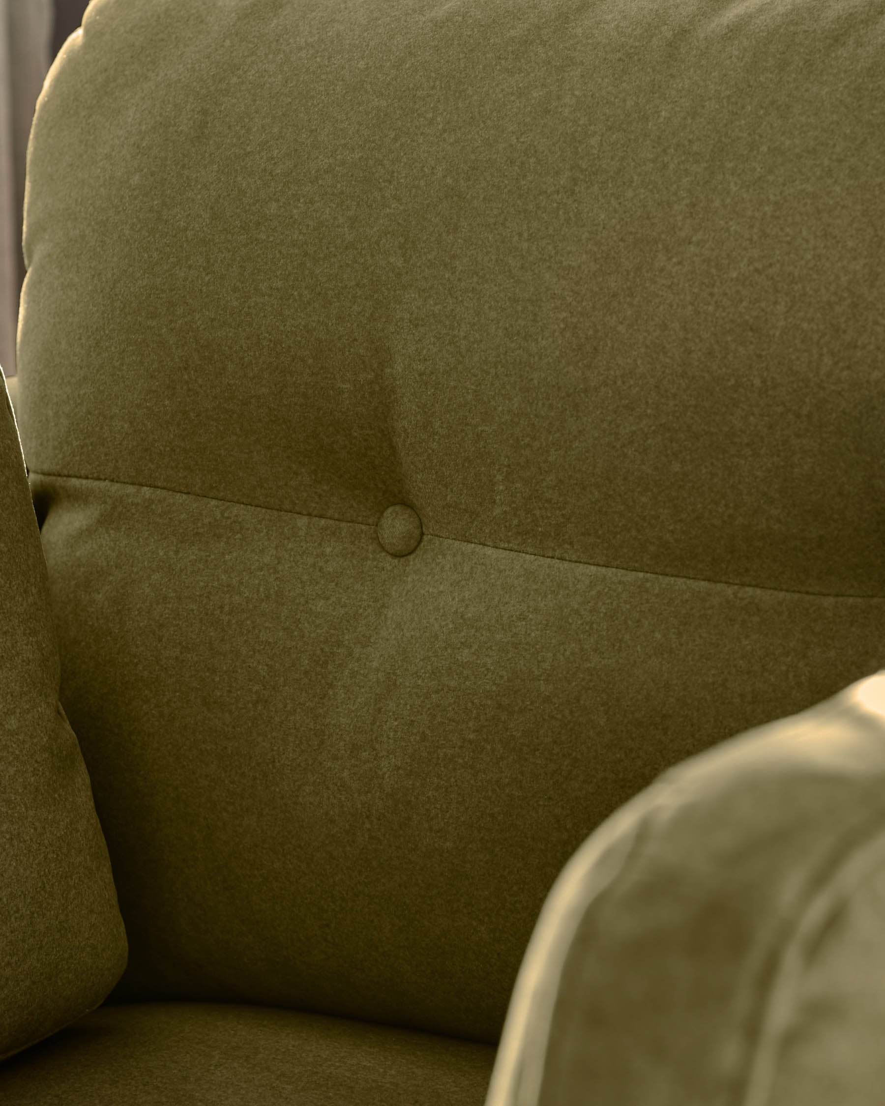 Delilah armchair in pistachio green fabric, showing close-up of seat back with button detail and curved armrest.