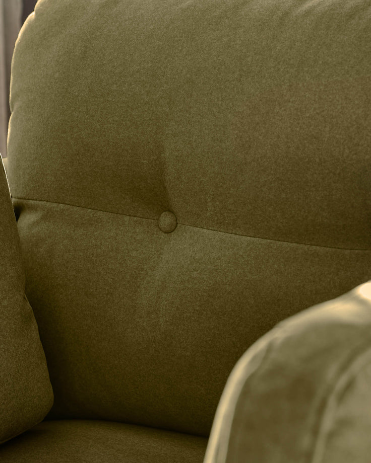Delilah armchair in pistachio green fabric, showing close-up of seat back with button detail and curved armrest.