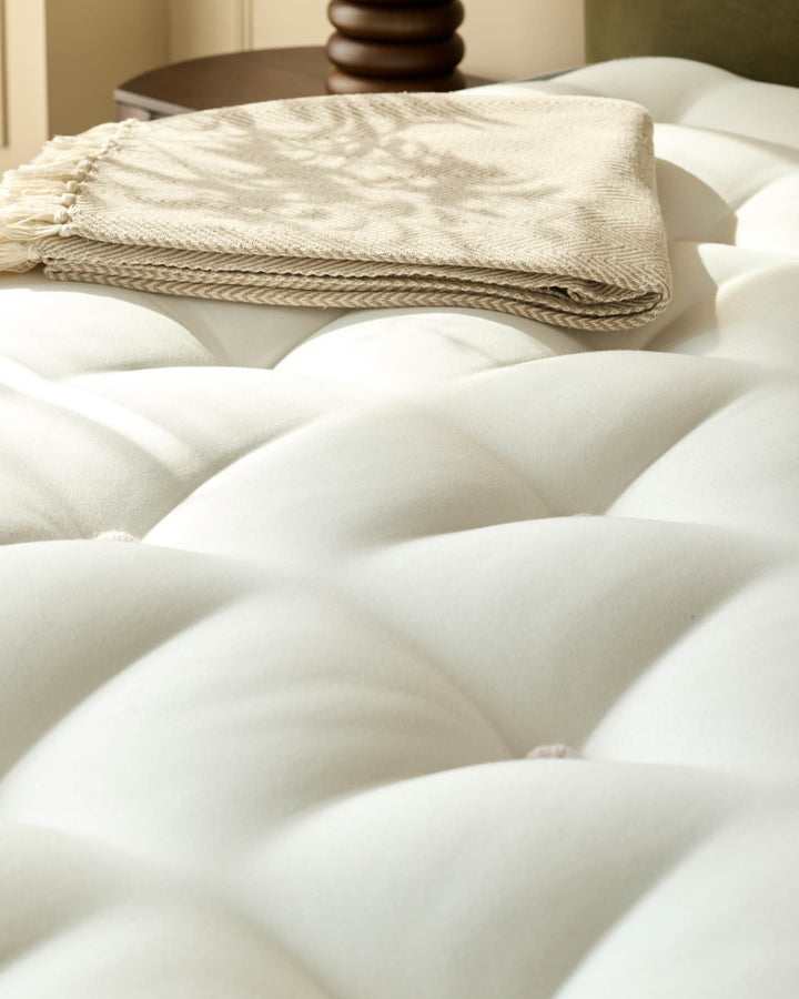 A luxurious mattress with a folded throw and wooden ornaments on a side table, creating a cosy bedroom scene.