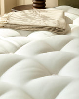 Close-up of a premium mattress featuring a tufted design and a folded throw blanket, evoking comfort and luxury.