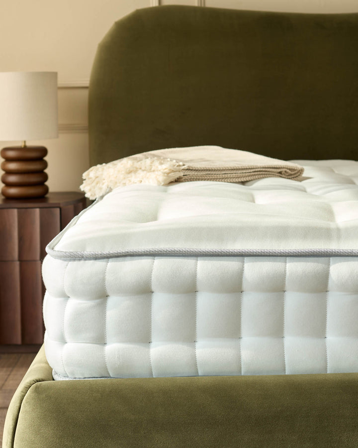Close-up of a stylish bed with an olive green headboard, a bedside table and neutral lamp.