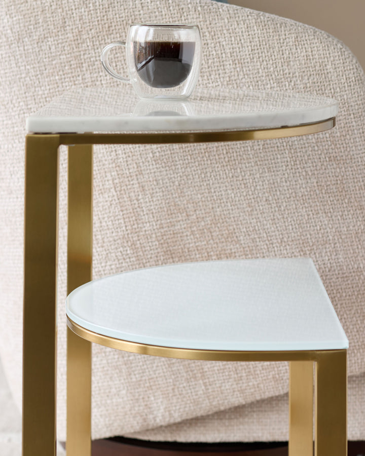 White marble demi-side table with brass frame and curved top, styled with a double-wall coffee mug against neutral fabric backdrop.