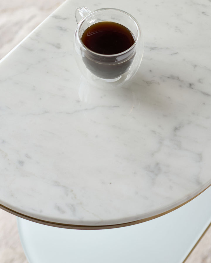 White marble demi-side table with natural veining, shown from above with a dark beverage in a glass cup for scale.