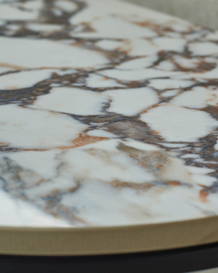 Close-up of a round marble table top with brown and grey veining and a gold edge.
