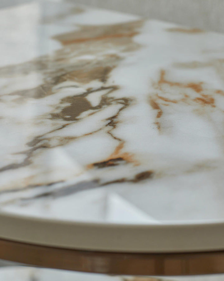 Close-up of a stylish marble-effect round side table with light brown trim and brass accents.
