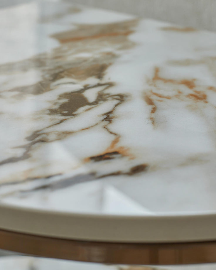 Close-up of a stylish marble-effect round side table with light brown trim and brass accents.