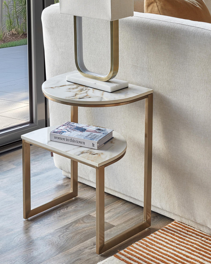 A two-tier side table with a marble top and gold-coloured metal frame. The table features a book on its bottom tier.