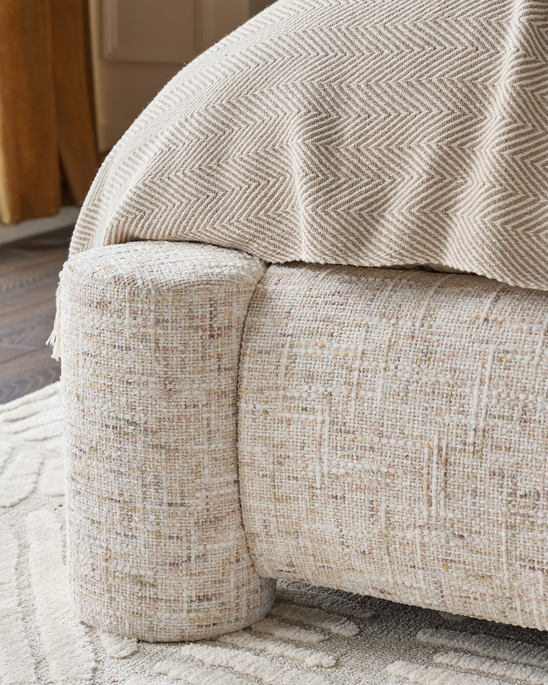 Deven king-size ottoman bed in natural fabric, close-up of curved cylindrical foot detail and herringbone pattern cushion.