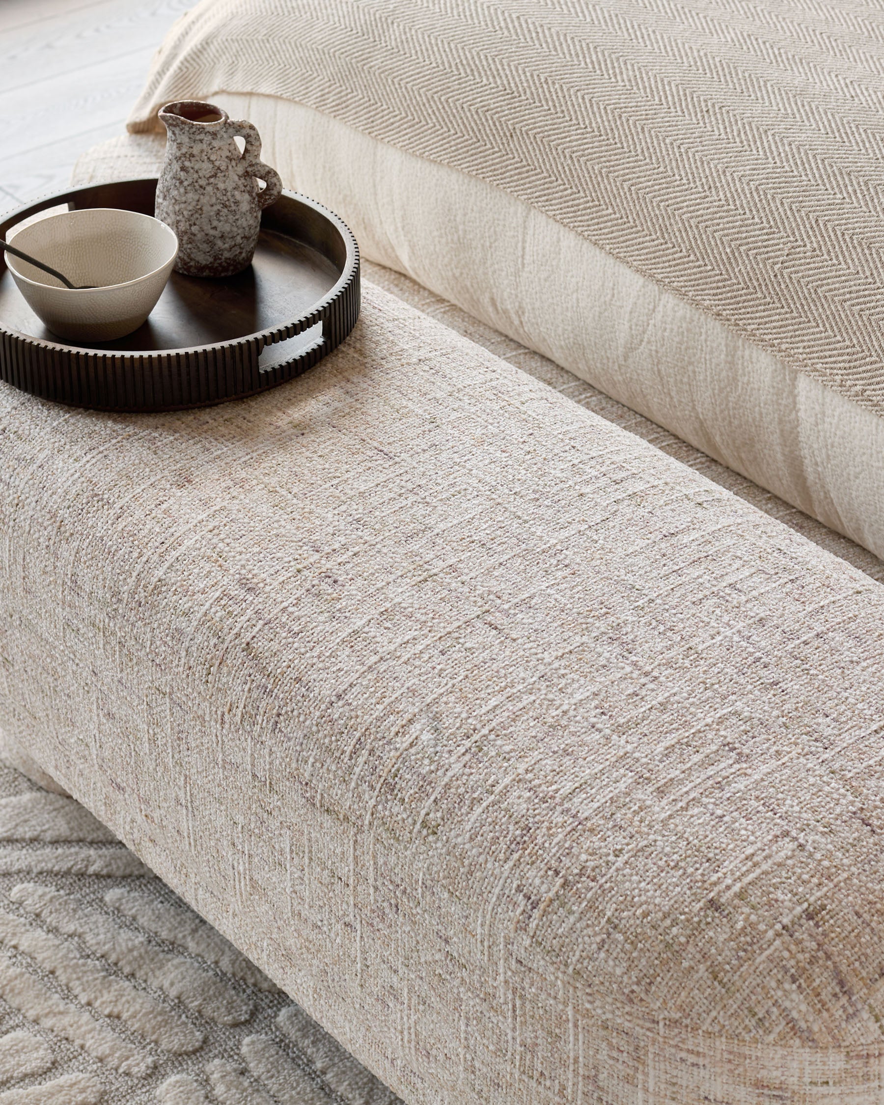 Deven upholstered bench in natural fabric, shown at an angle with decorative tray and ceramic accessories on top.