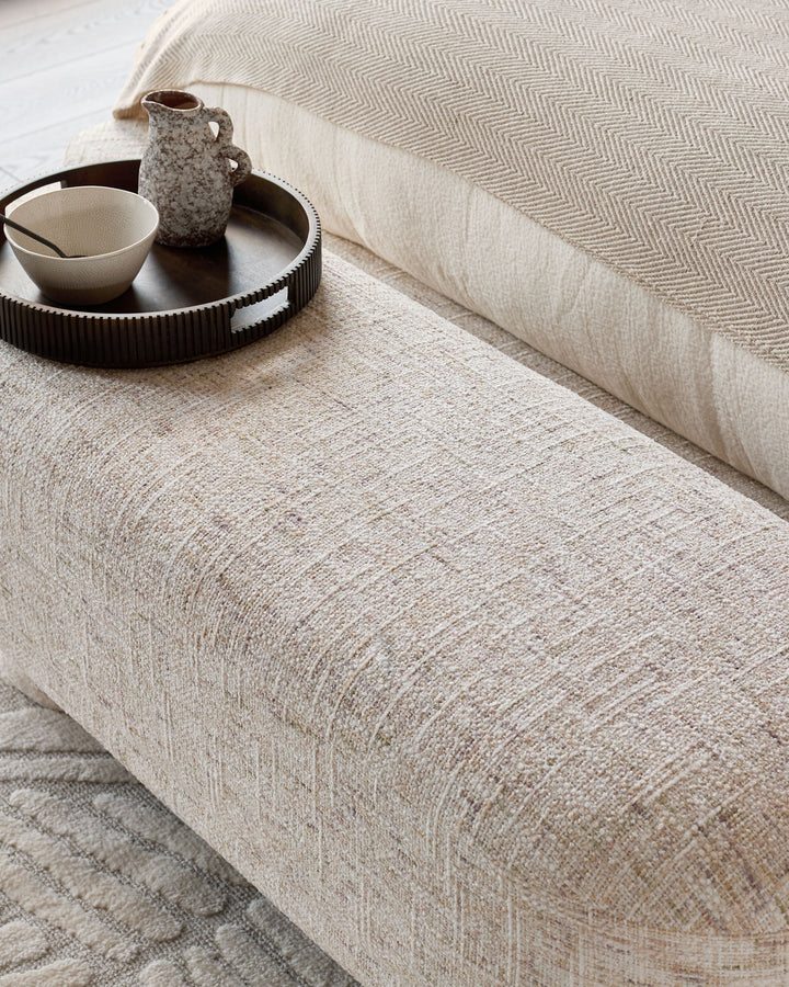 Deven upholstered bench in natural fabric, shown at an angle with decorative tray and ceramic accessories on top.