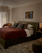 Deven king-size ottoman bed in olive-green velvet, styled in a modern bedroom with burgundy bedding and patterned cushions.