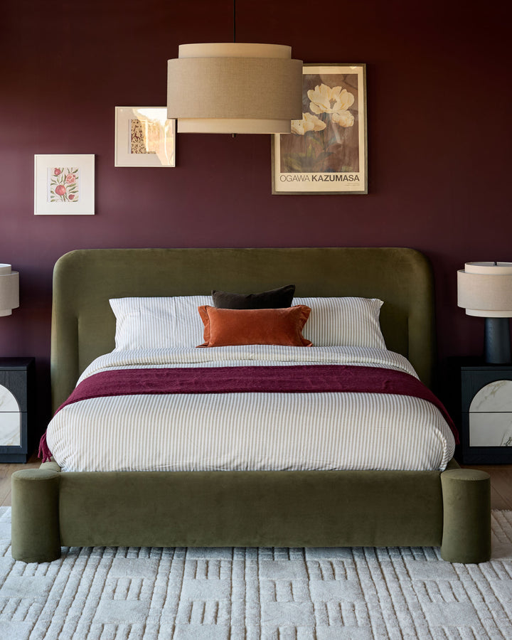 Deven king-size ottoman bed in olive-green velvet with rounded headboard and footboard, styled in burgundy bedroom.
