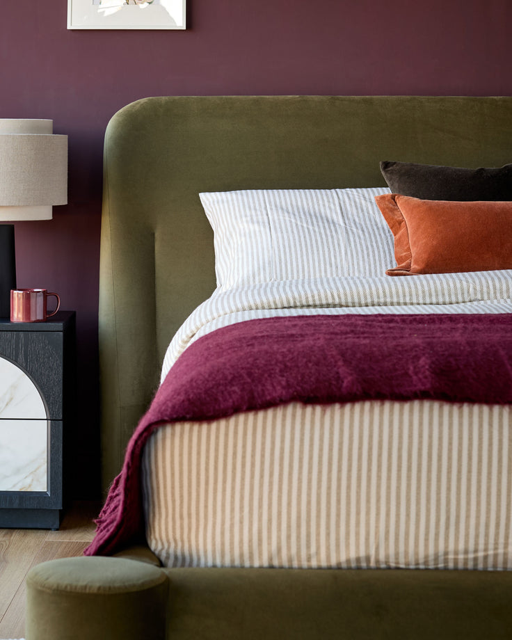 Deven king-size ottoman bed in olive-green velvet with rounded headboard, styled with colorful bedding and pillows.