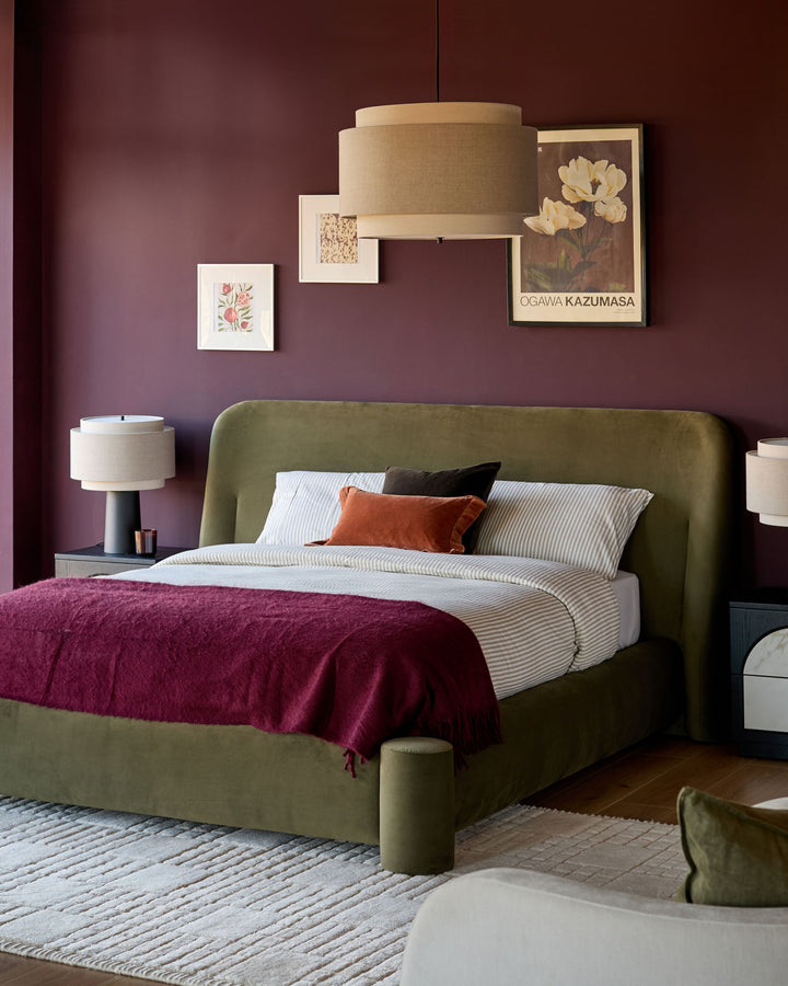 Deven king-size ottoman bed in olive-green velvet, shown in a styled bedroom with burgundy walls and coordinating furnishings.