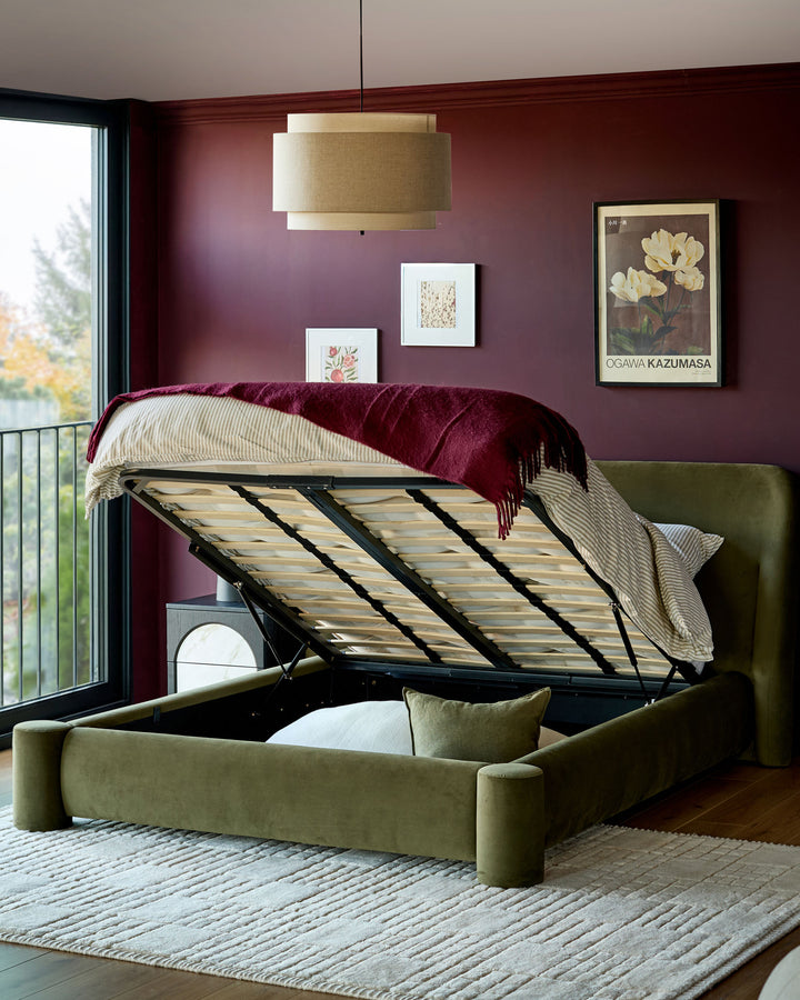 Deven King-Size Ottoman Bed in olive green velvet with storage compartment open, displaying wooden slat base in modern bedroom.