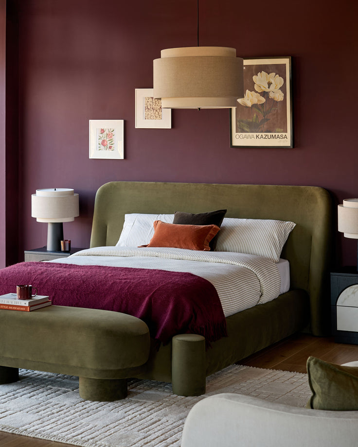 Deven king-size ottoman bed in olive-green velvet with curved headboard and footboard, styled in a burgundy bedroom.