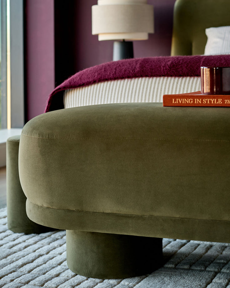 Deven bench in olive-green velvet, curved cylindrical shape, shown in living room setting with styled accessories.
