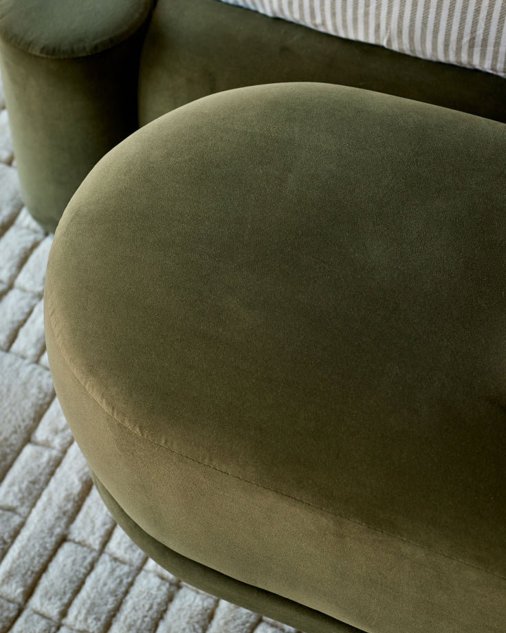 Deven bench in olive-green velvet, showcasing curved, rounded shape from top angle on textured cream rug.