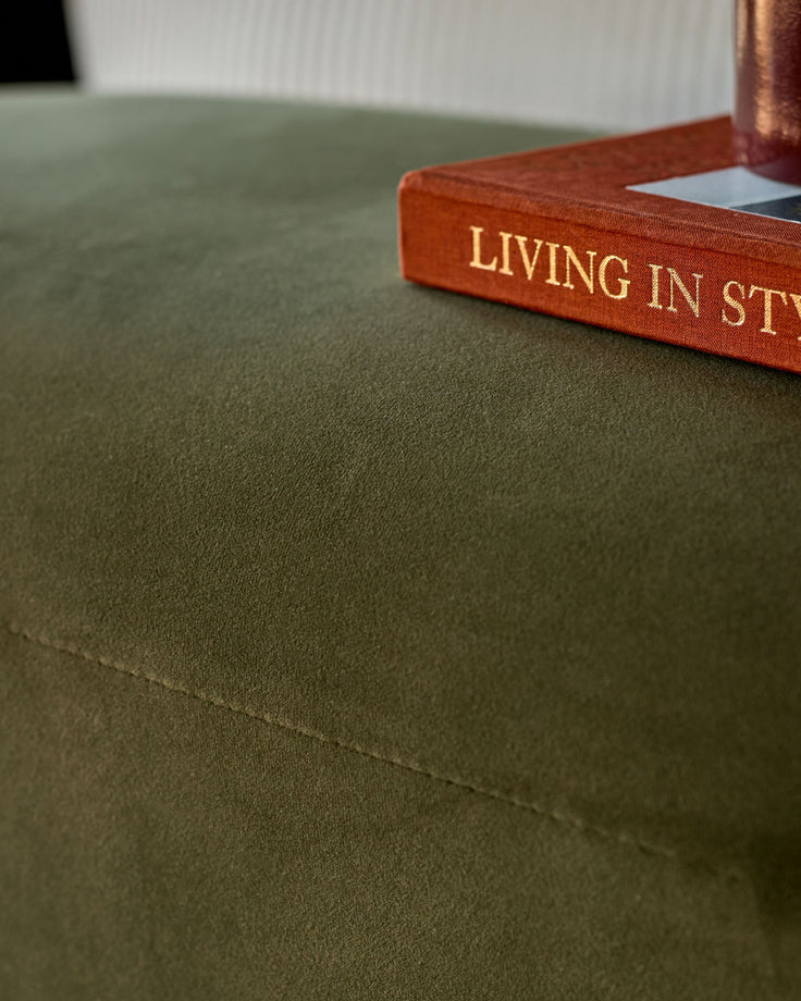 Deven bench in olive green velvet with a decorative book placed on top, shown in close-up angle detail.