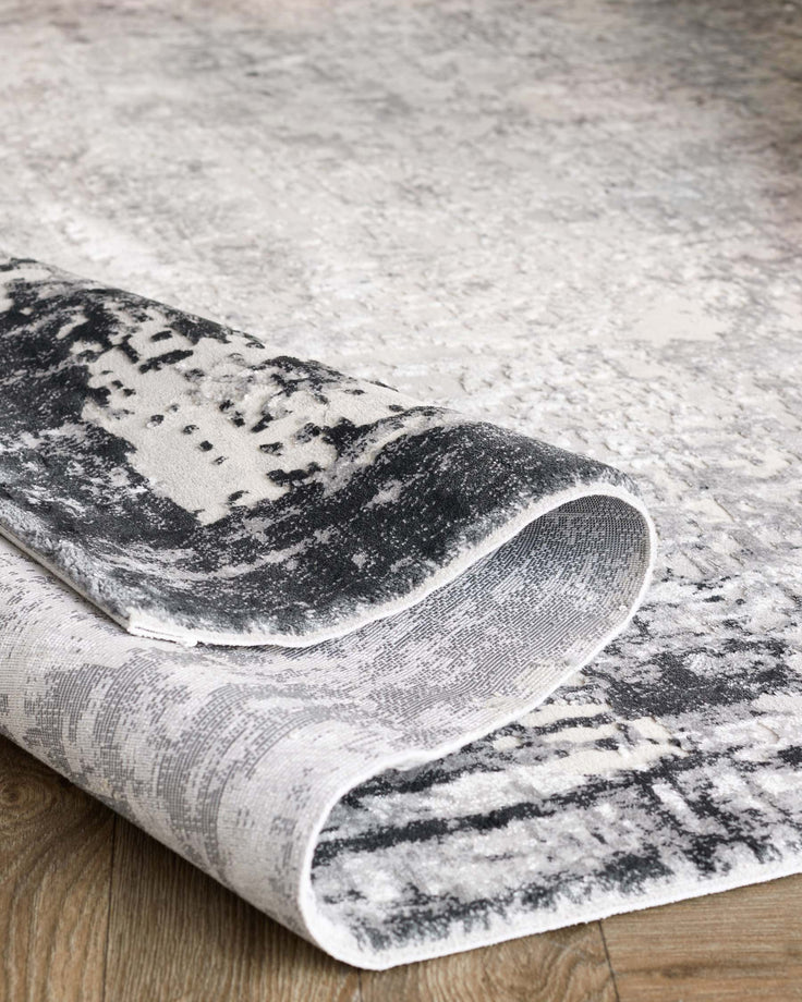 A grey abstract design rug with a curled edge, revealing its patterned texture.
