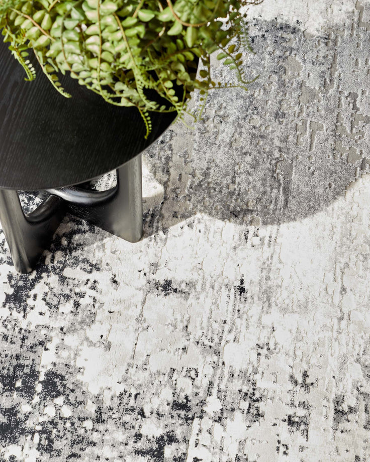 A close up shot of a modern black wooden side table with a dark grey patterned rug beneath it, and a houseplant on top.