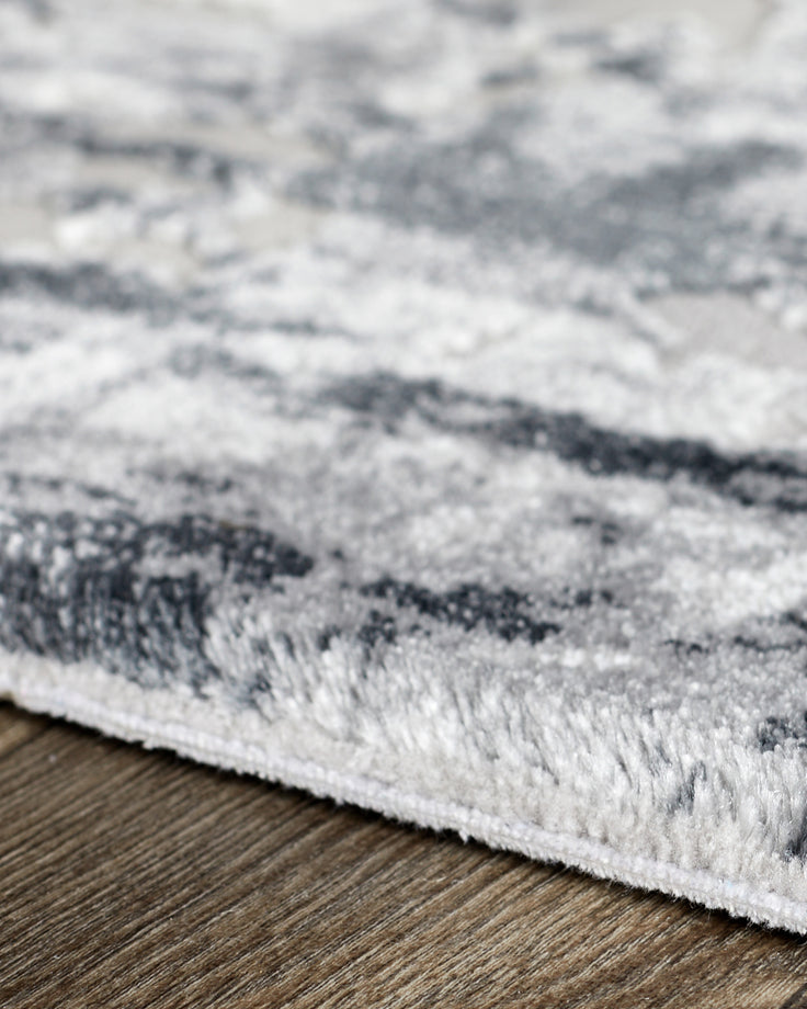 Distressed border large textured rug in grey on wood flooring, close-up detail view.