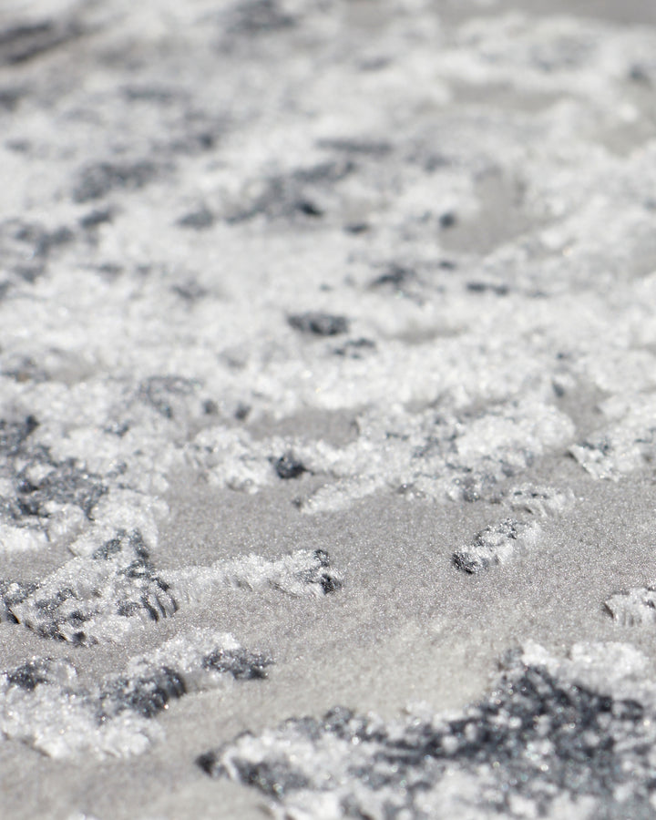 Close-up of grey distressed textured rug showing raised fibres and mottled surface pattern detail.