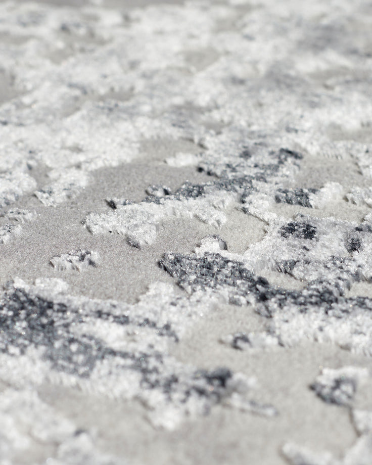 Close-up of grey textured rug surface showing distressed, mottled finish with white and grey tones and subtle variations in pile height.