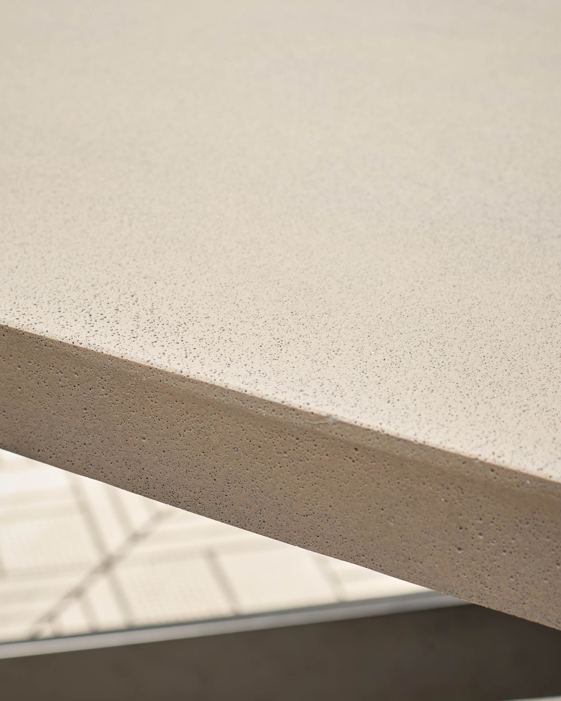 Close-up of concrete tabletop surface showing speckled light grey finish and edge detail with metal frame.