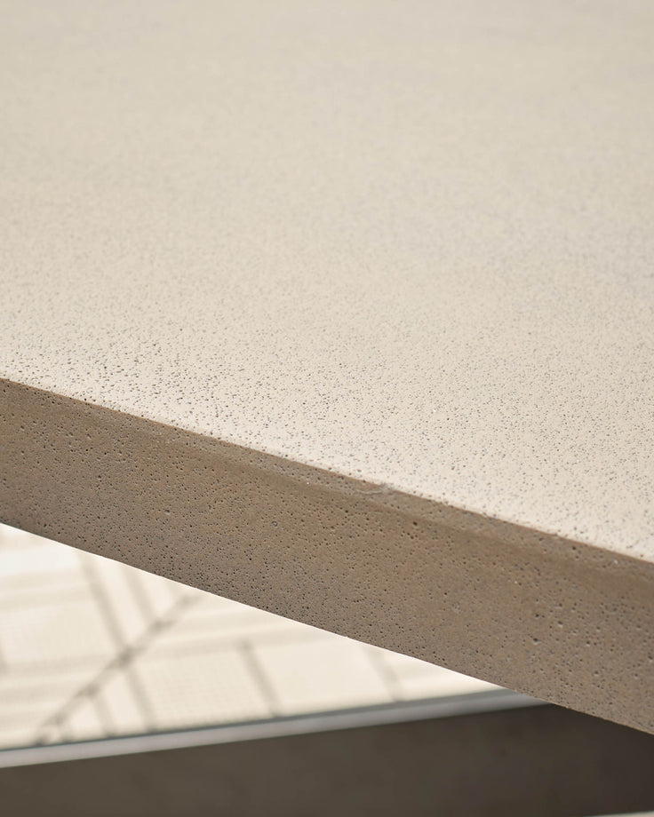 Close-up of concrete tabletop surface showing speckled light grey finish and edge detail with metal frame.