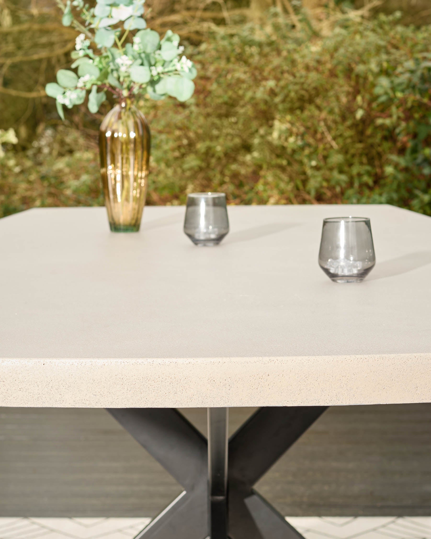 Donato garden dining table with light stone top and dark grey pedestal base, styled with glasses and flowers.