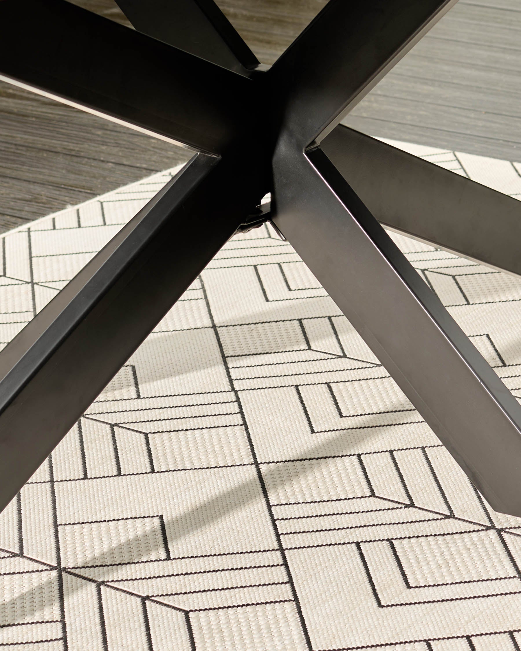 Dark grey dining table base with black metal X-frame legs on patterned carpet, angled view.