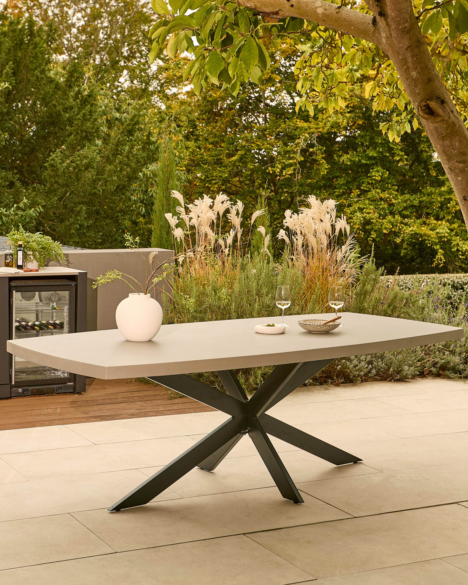 Donato garden dining table with dark grey spider-leg base and light grey top, styled in outdoor patio setting.