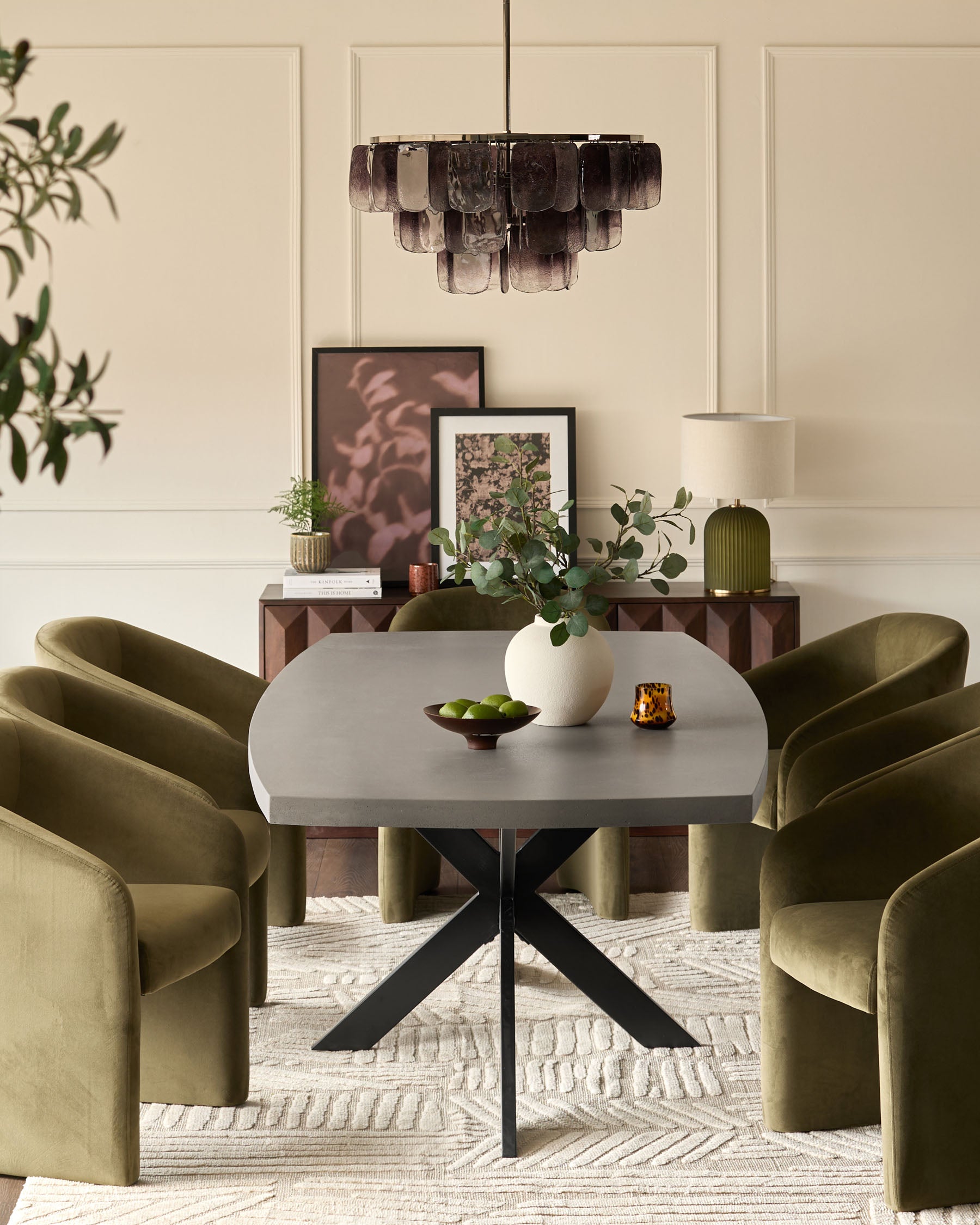 Round grey dining table with black X-frame base, styled in modern dining room with olive green chairs.