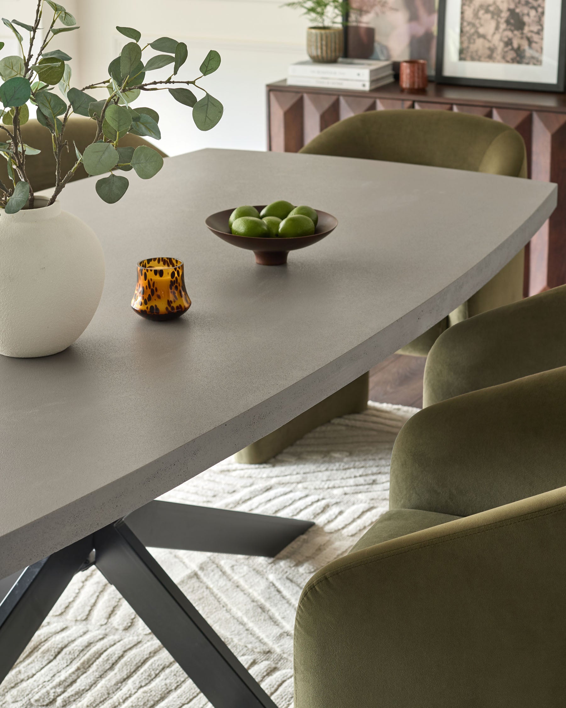 Donato dark grey dining table with light concrete top and black X-frame base, styled with green chairs and accessories.