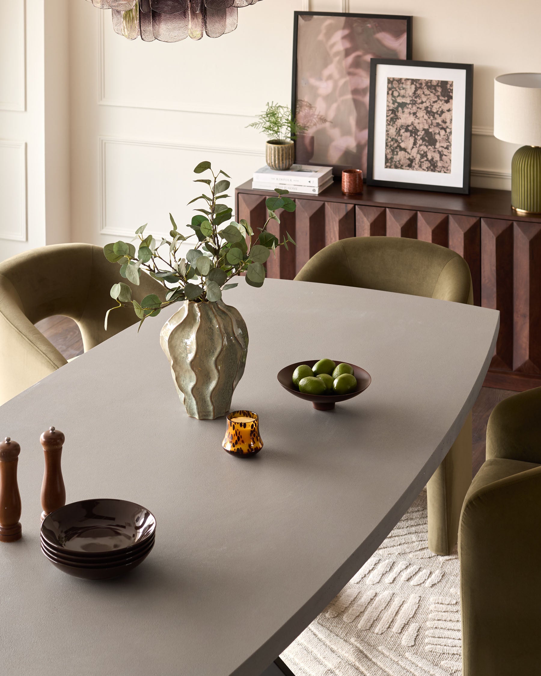 Dark grey dining table with natural wood finish, styled with green upholstered chairs and decorative accessories in a modern dining room setting.