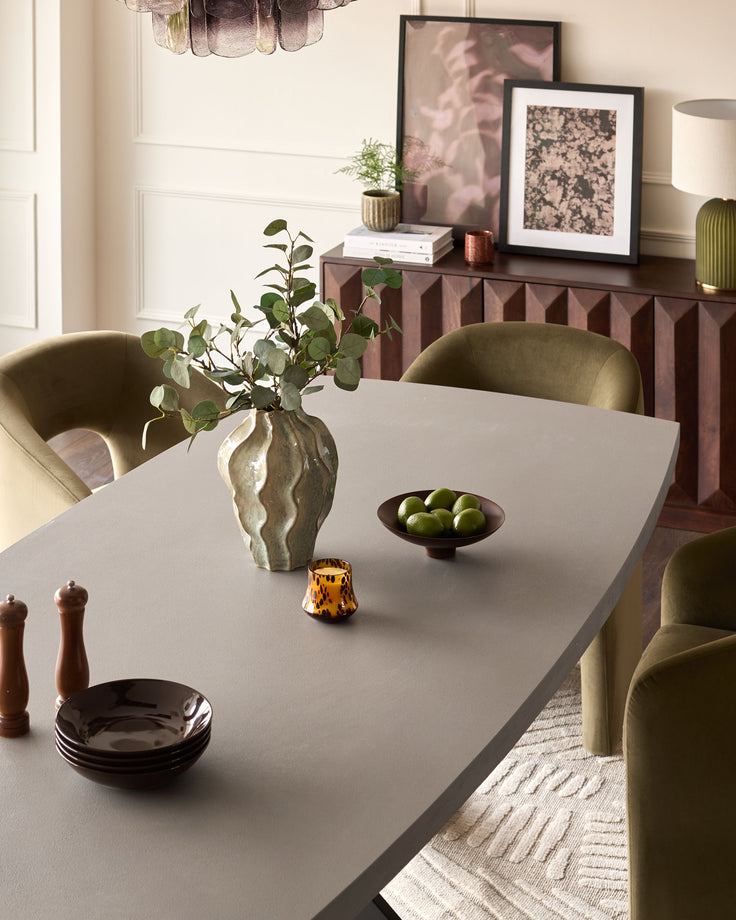 Dark grey dining table with natural wood finish, styled with green upholstered chairs and decorative accessories in a modern dining room setting.