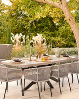 Donato dark grey 10-seater dining table set outdoors with woven chairs and place settings under tree shade.