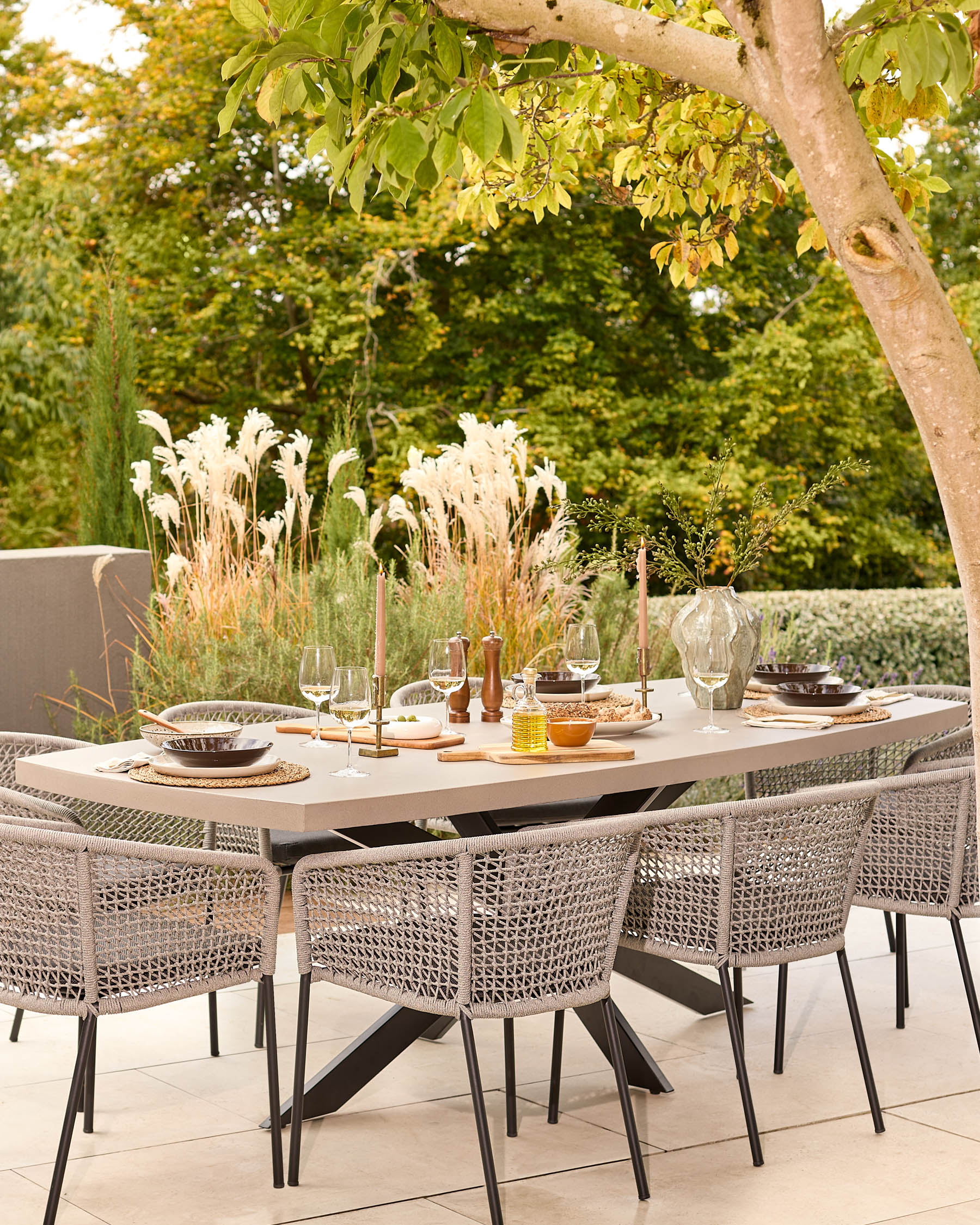 Donato dark grey 10-seater dining table set outdoors with woven chairs and place settings under tree shade.