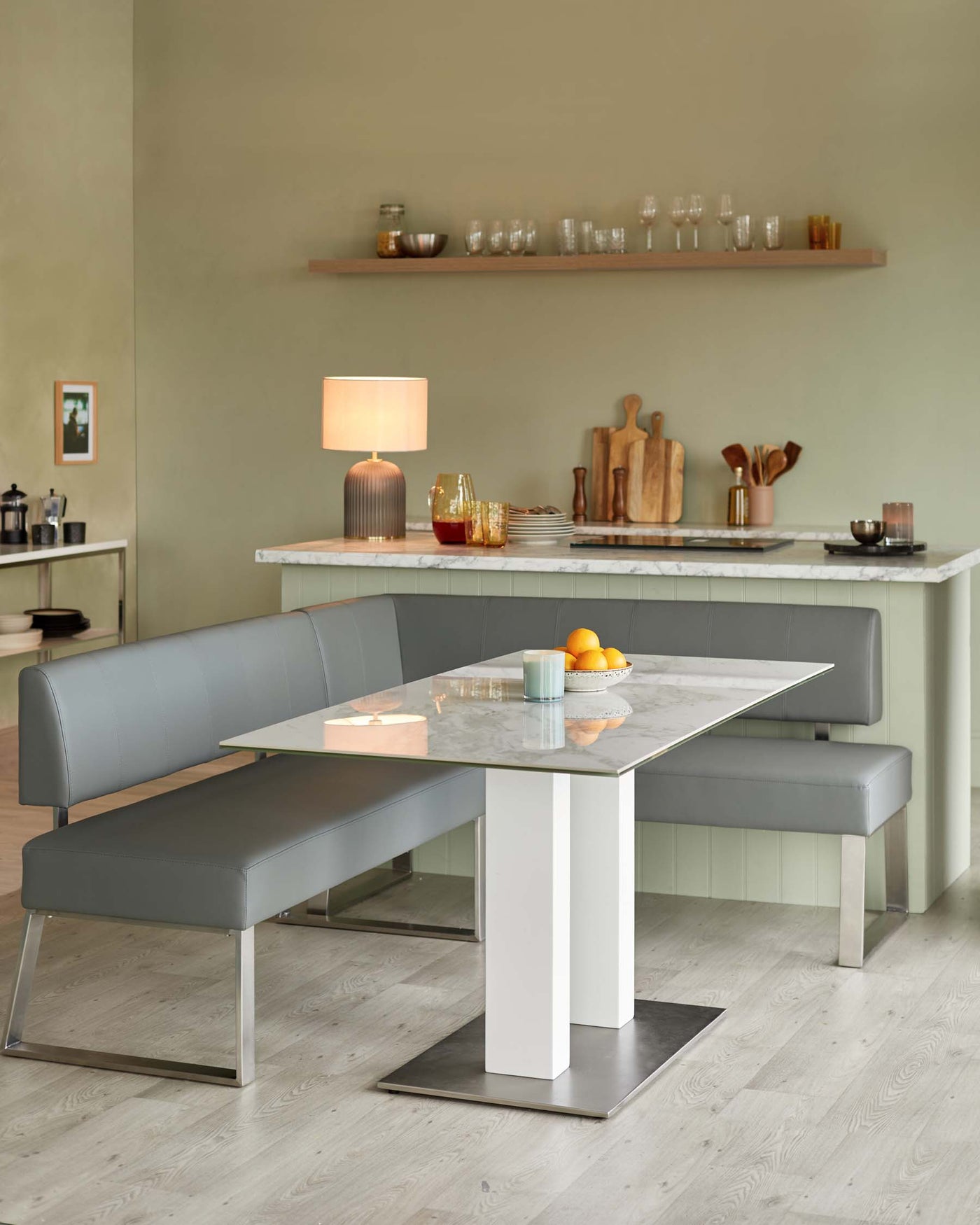Modern dining set featuring a rectangular marble-top table with a white and stainless steel base, paired with a grey upholstered L-shaped bench and a matching grey upholstered bench, all positioned on a light wooden floor.