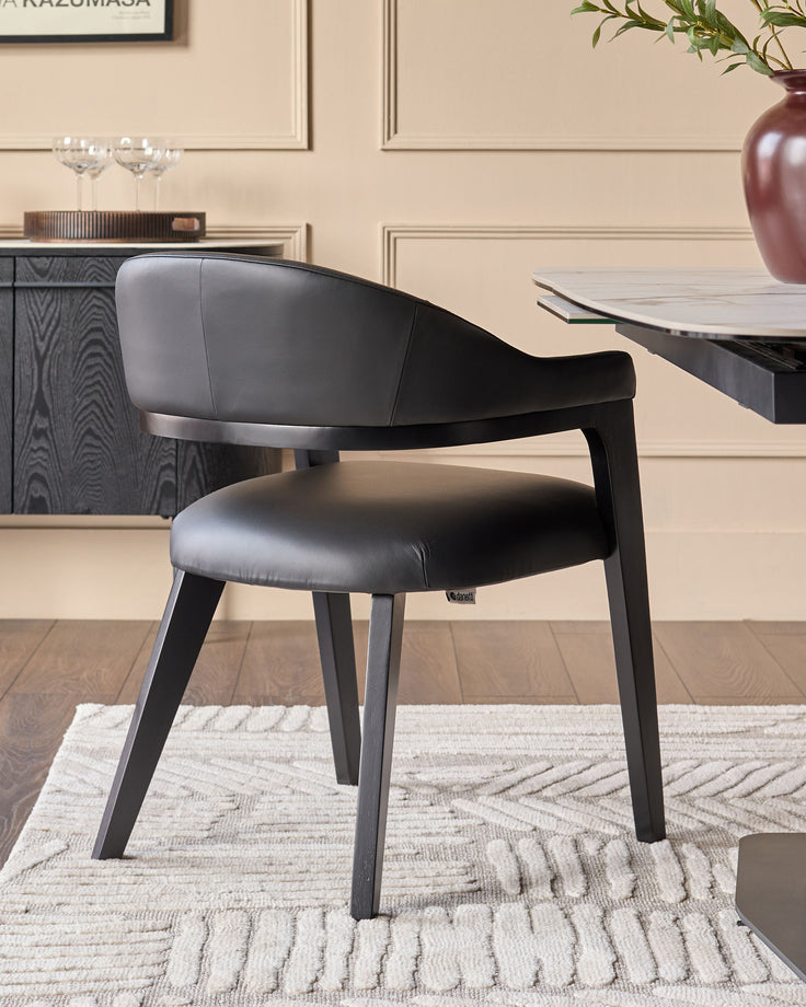 Dylan dining chair in black leather with curved backrest and black wooden legs, shown in a modern dining setting.