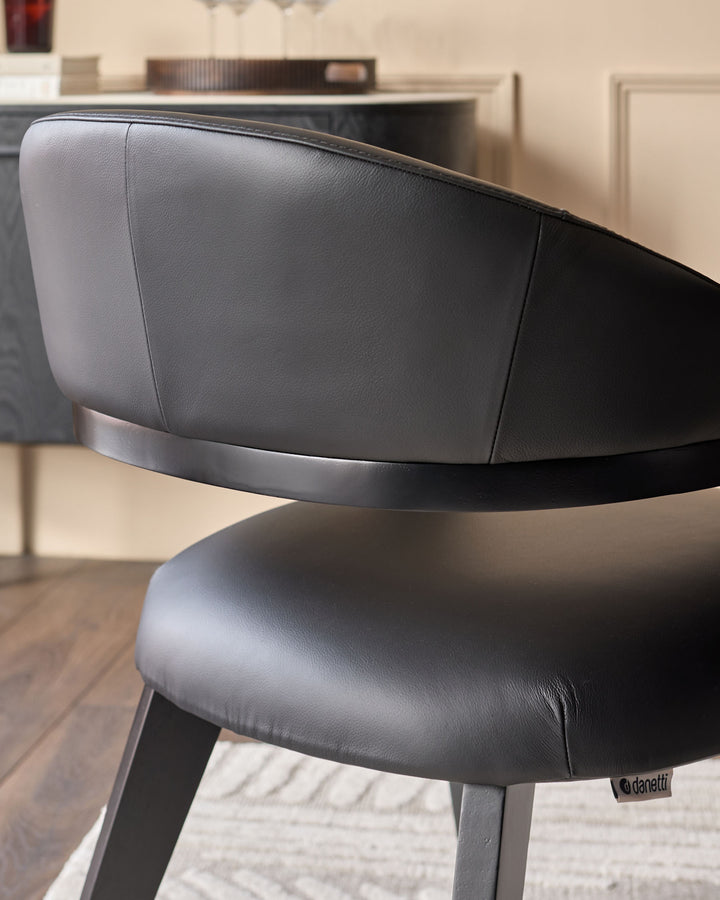 Dylan dining chair in black leather, shown from a side angle highlighting the curved backrest and seat cushioning.