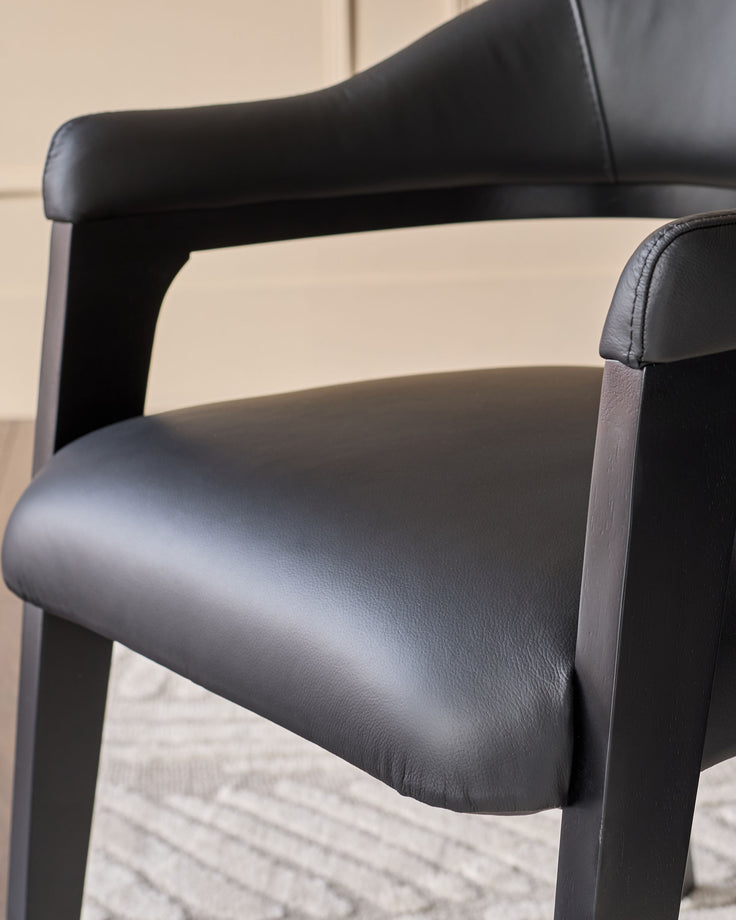 Dylan dining chair in black leather, side view showing curved backrest and armrests with dark wood frame.