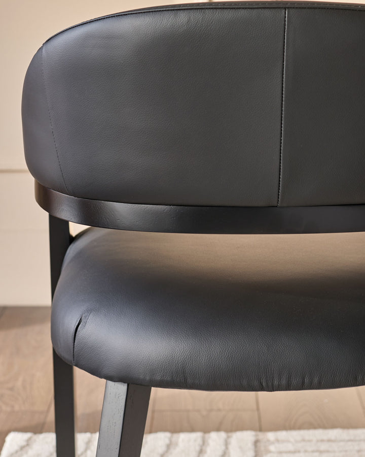 Dylan dining chair in black leather, side angle view showing curved backrest and dark metal frame legs.