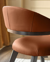 Tan leather Dylan dining chair shown from side angle, featuring curved backrest, dark metal frame band, and wooden legs with Danetti branding.