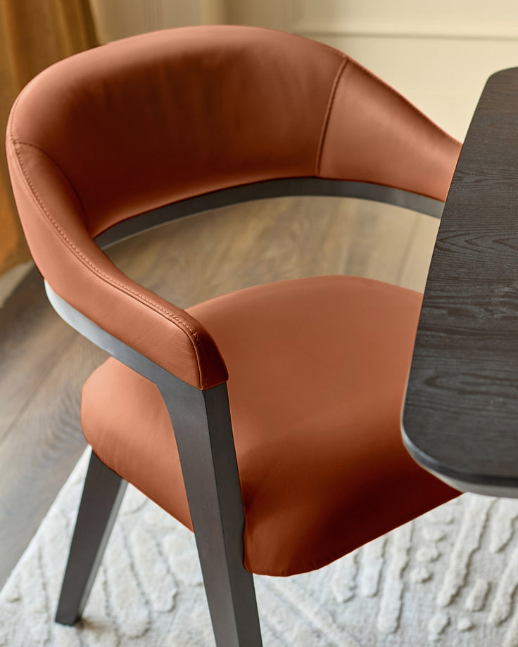 Dylan dining chair in tan leather with dark wood frame, side view showing curved backrest and armrests.