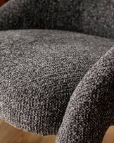 Close-up of dark grey upholstered dining chair showing textured fabric weave and curved seat detail.