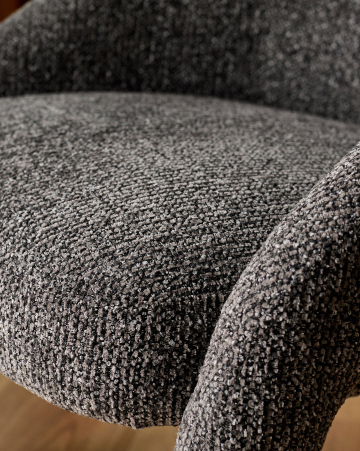 Close-up of dark grey upholstered dining chair showing textured fabric weave and curved seat detail.